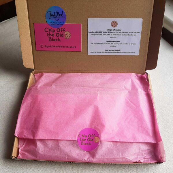 Box of cookies wrapped in pink tissue paper with pink logo sticker, pink business card and allergen information stuck to inside of box